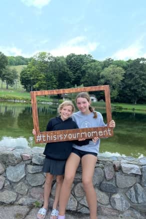 Two girls posing and holding a frame that says "This is Your Moment" at The Highlands