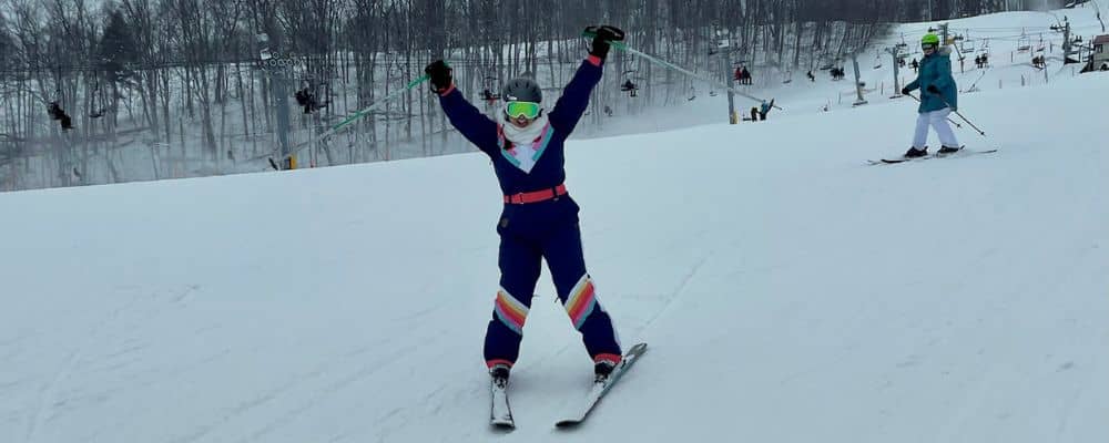 Woman in snowsuit skiing with arms in the air